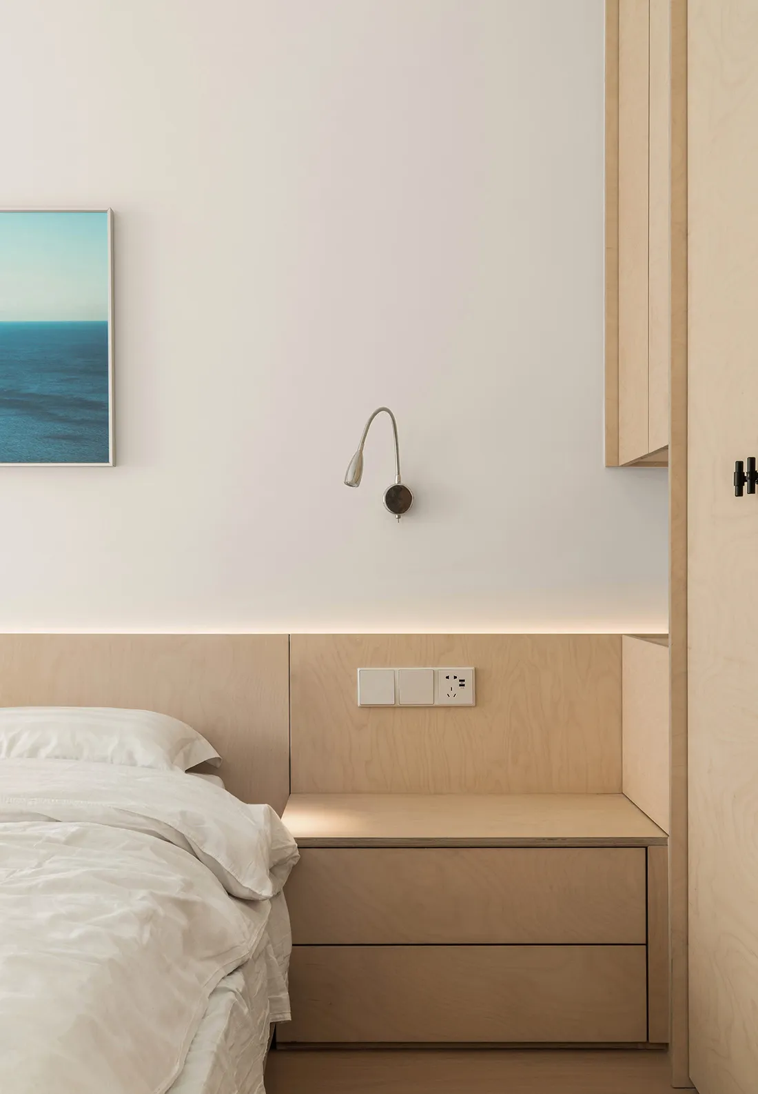 A modern minimalist bedroom featuring wooden furniture and a light blue artwork.