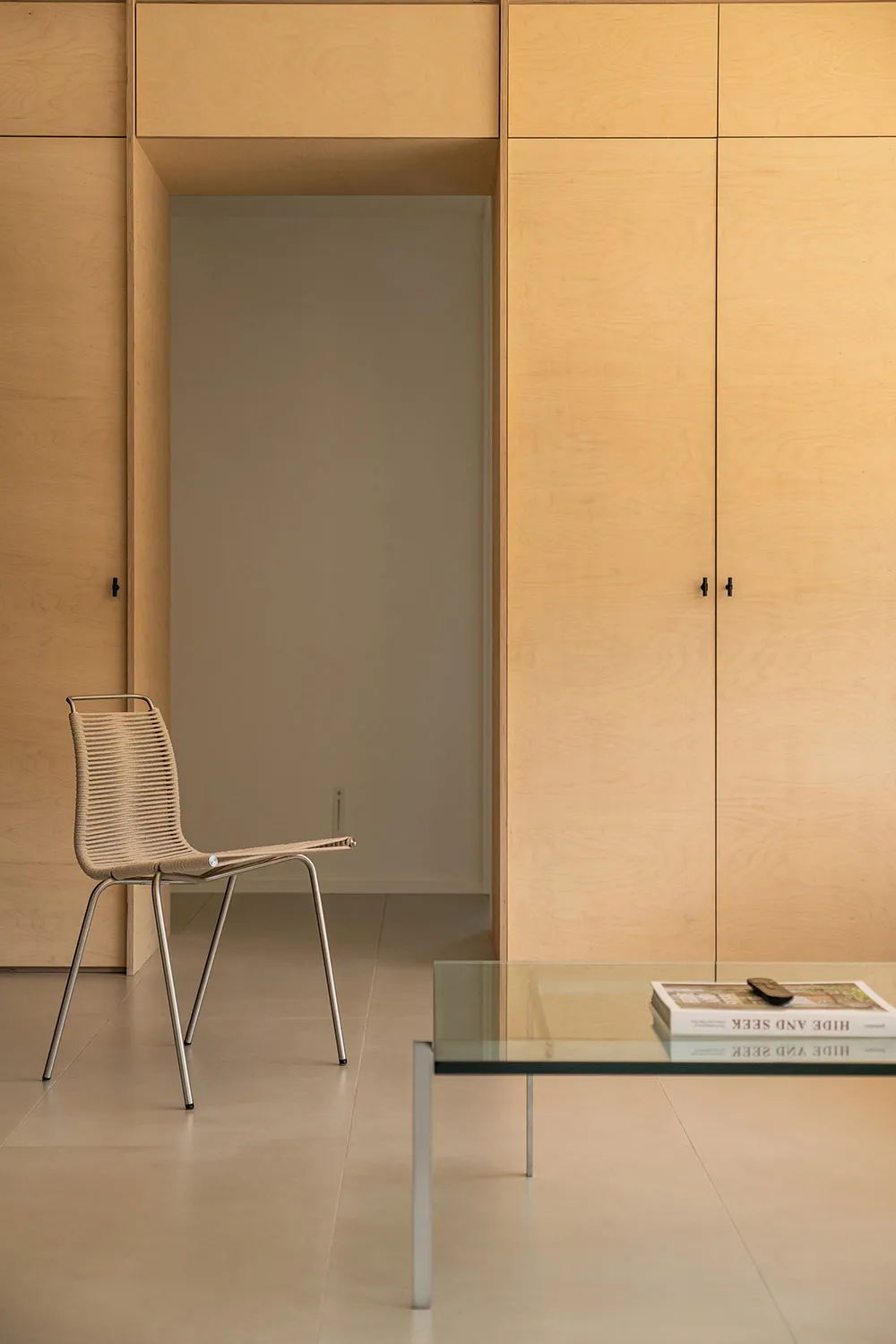 Modern interior space featuring minimalist, sleek wood cabinets and a glass coffee table with books and a remote.