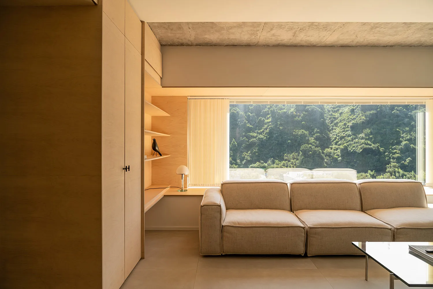 A modern living room with a compact design, featuring a beige sectional sofa, wooden shelves, and a glass coffee table with a