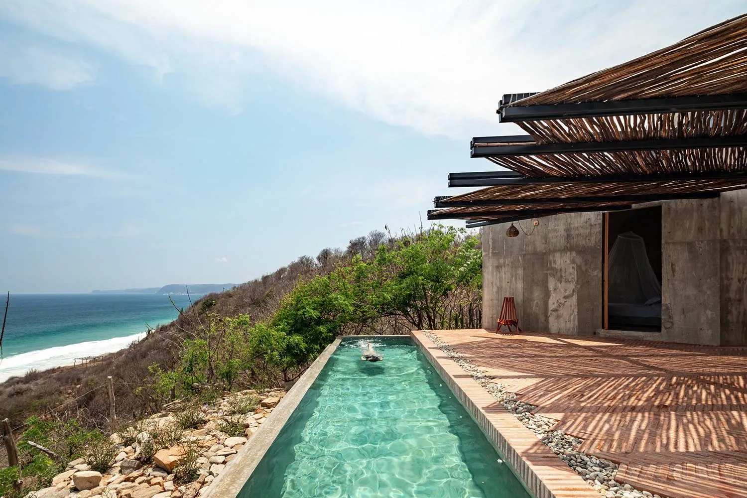 Modern minimalist residential building with a concrete and wood exterior featuring a small rectangular pool with clear water