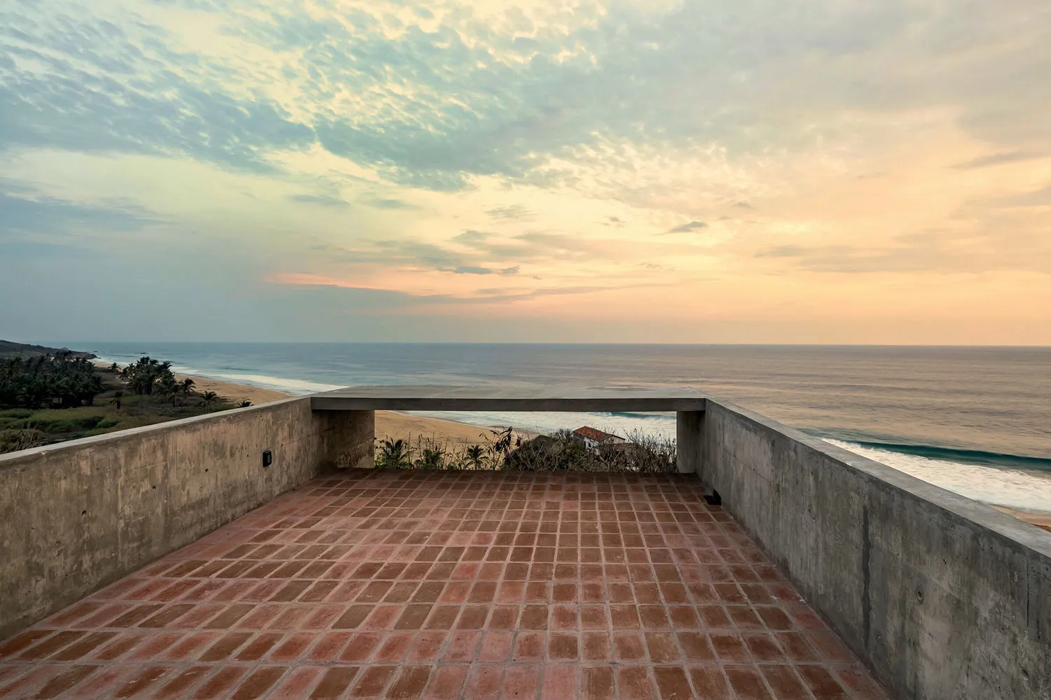 Concrete terrace overlooking the sea with red brick tiles on the floor.