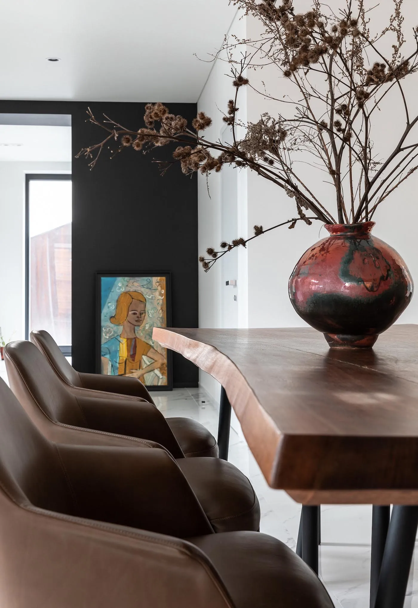 A modern dining room featuring a wooden table adorned with a large, decorative vase filled with dried flowers, and three brow