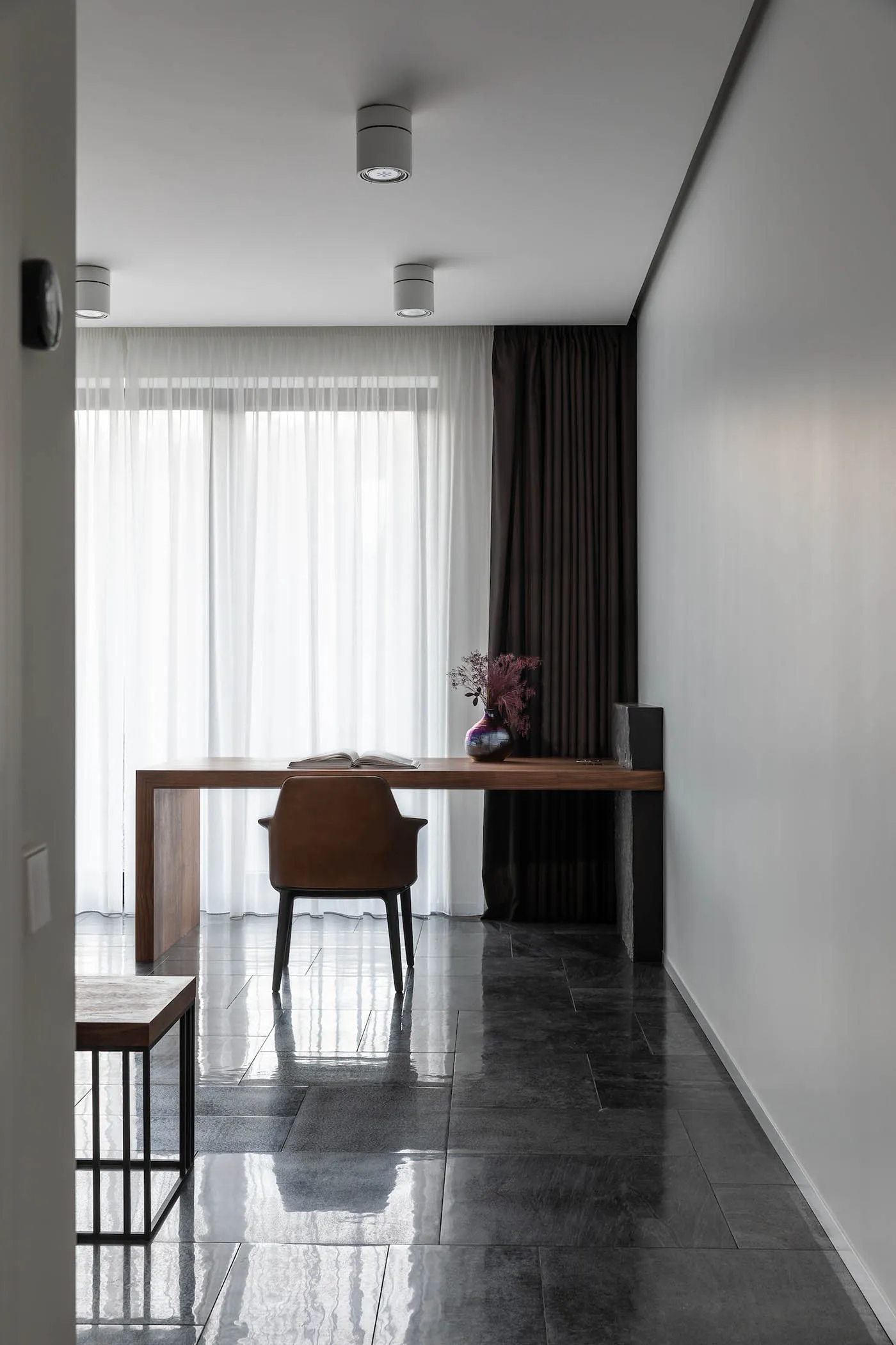 A minimalist home office with a wooden desk, glass panels, and a leather chair.