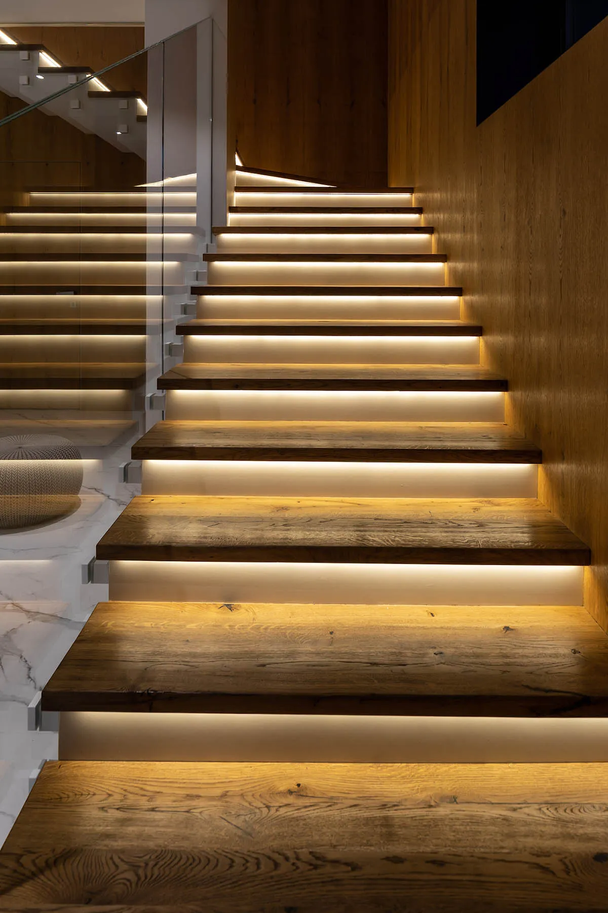 A modern staircase featuring wooden steps with recessed lighting on the underside of each tread for illumination.