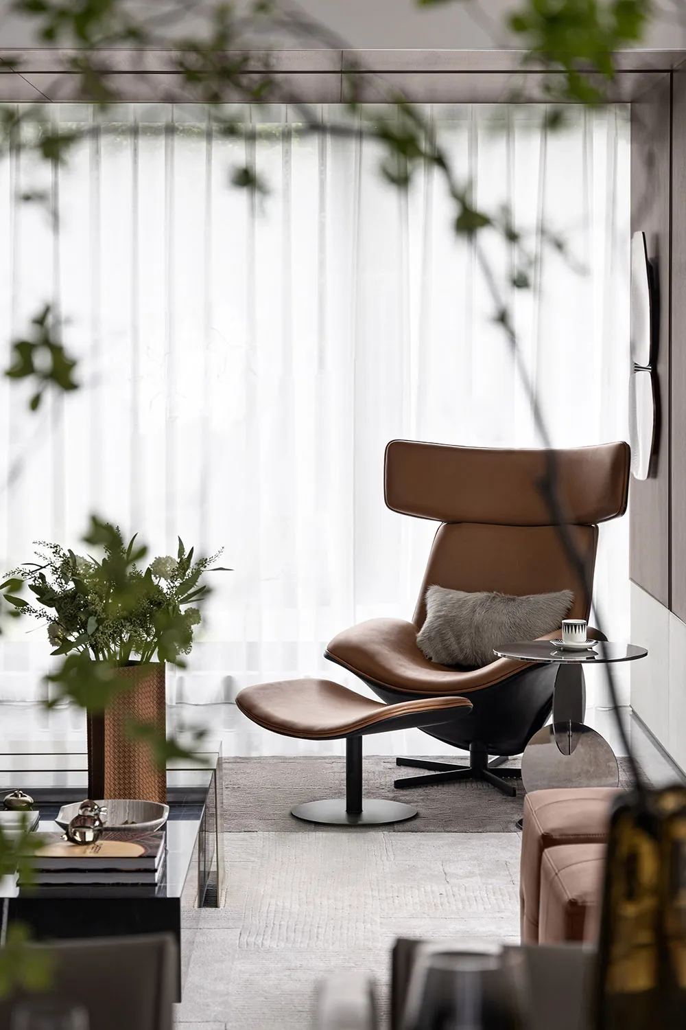A modern living room with a cozy brown leather armchair and ottoman, featuring minimalistic decor and plush cushions.