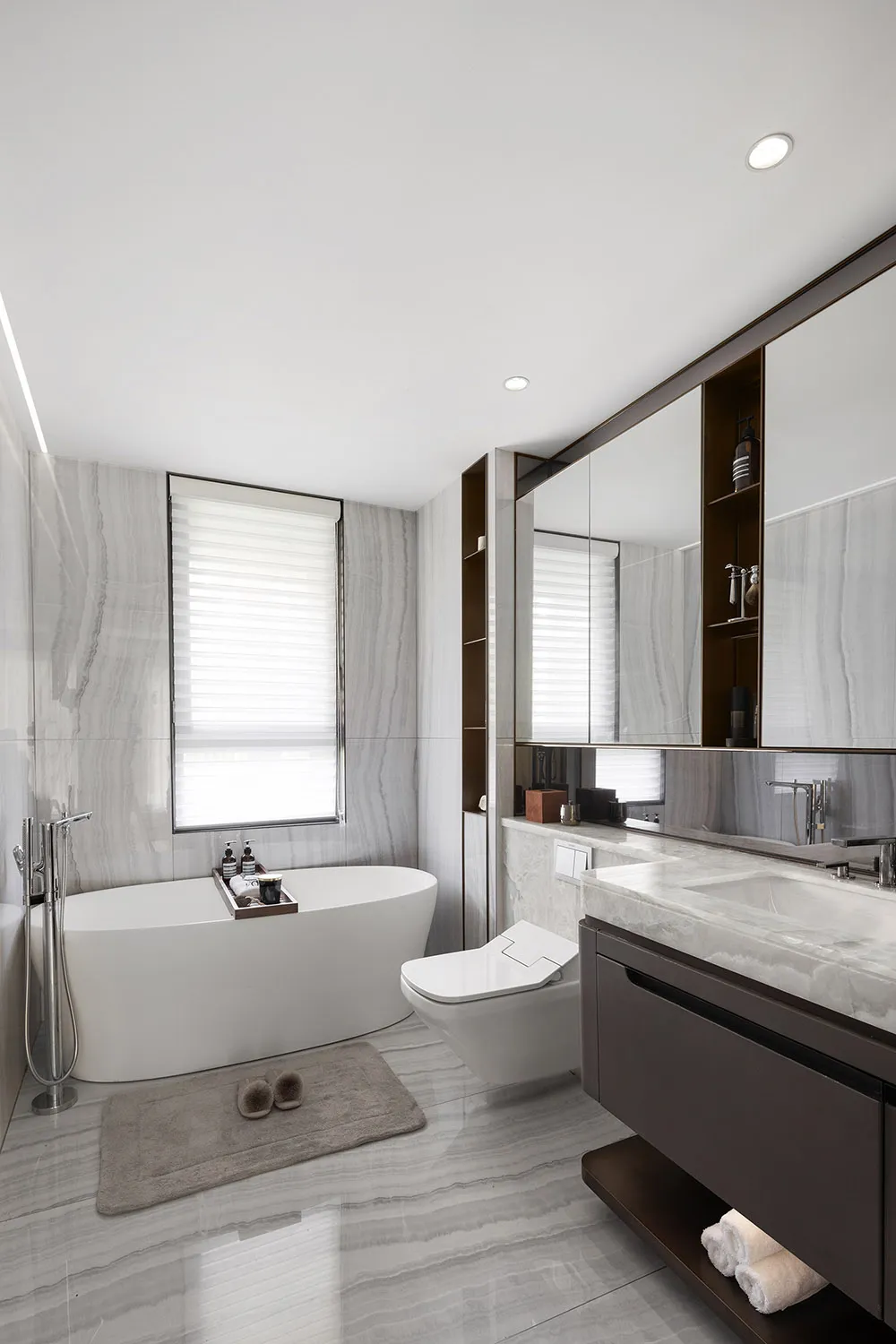 A modern bathroom featuring a freestanding tub, toilet, and vanity with a large mirror.
