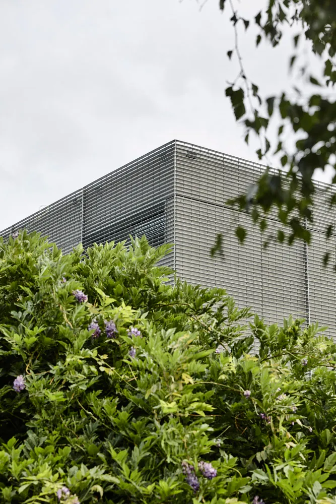 A modern building with a metallic frame and greenery in the foreground.