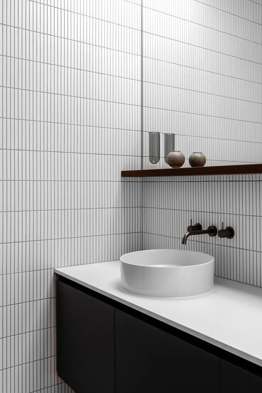 Modern minimalist bathroom with white tiled walls, black cabinets, and a white porcelain sink.