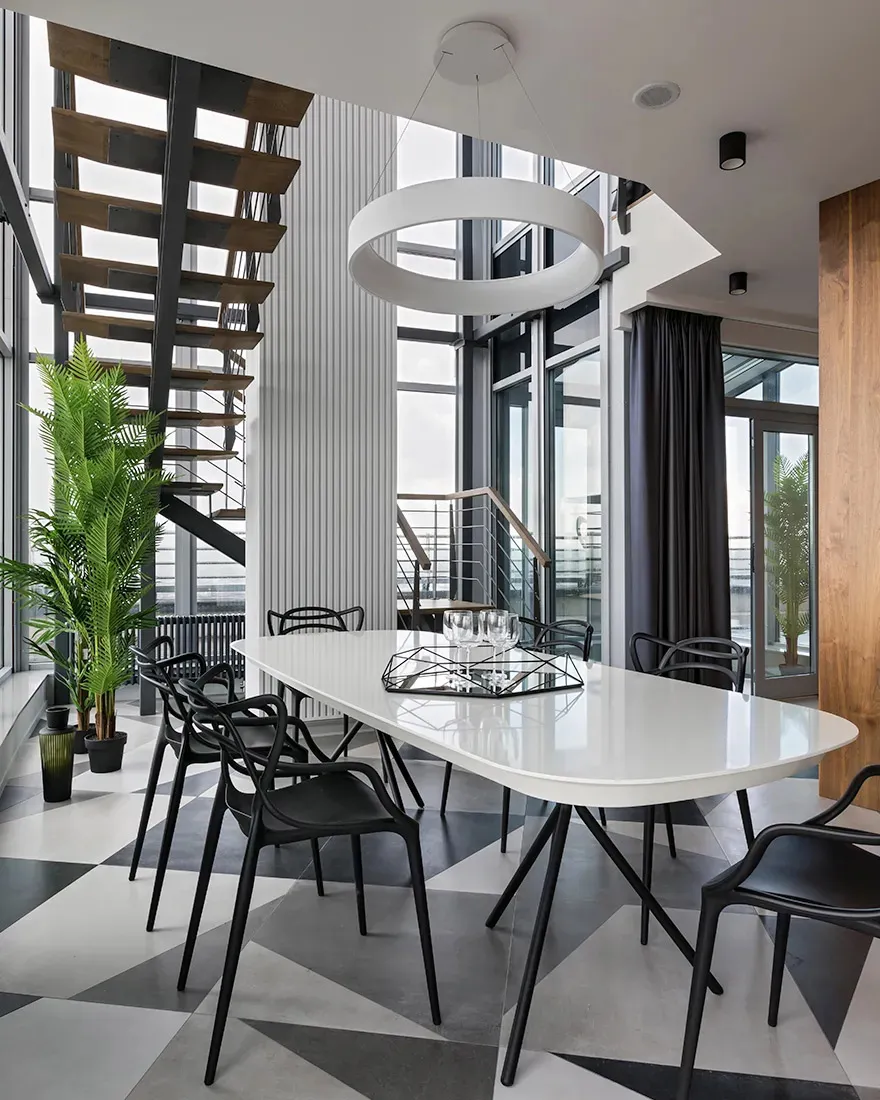 Modern dining room featuring a white oval table with black legs surrounded by black chairs on a geometric floor, illuminated