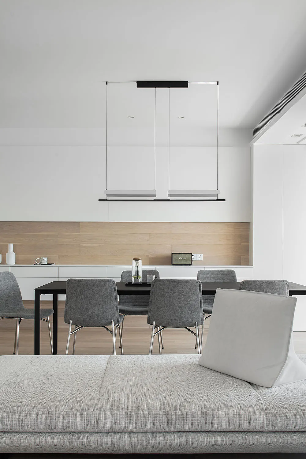 Modern dining room featuring a white minimalist interior design with a sleek dining table, grey chairs, and a hanging light f