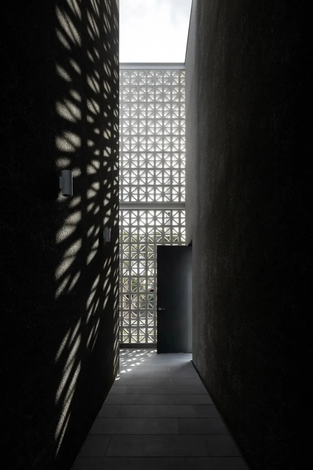 A corridor with concrete walls displaying geometric shadows created by a grid-like structure above.