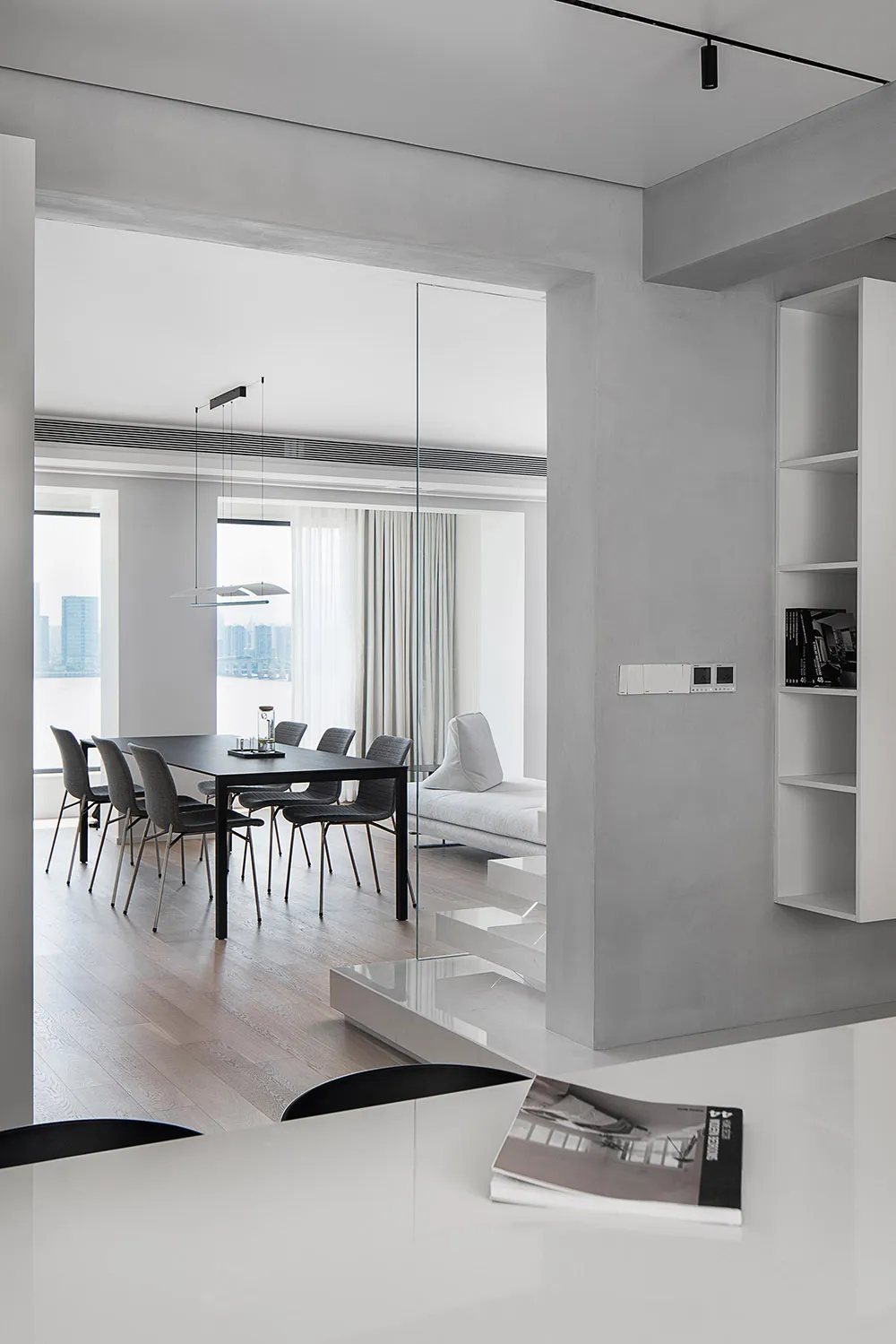 A modern minimalist dining room featuring concrete, glass, and wood materials with a black dining table and chairs.