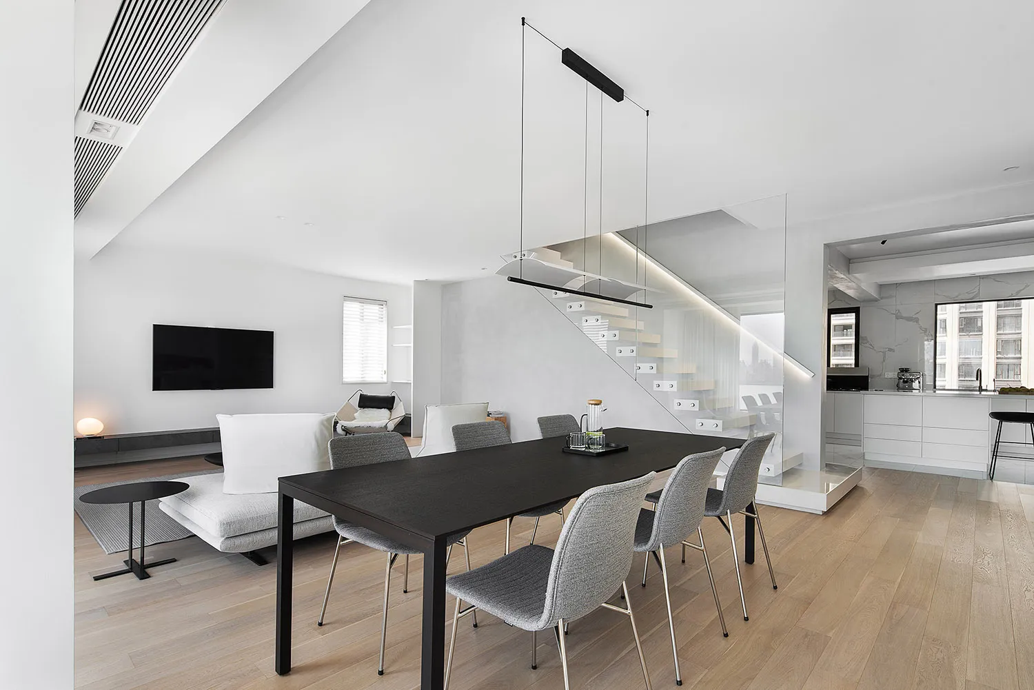 Contemporary living room with minimalist design, featuring a white couch, grey chairs, and natural wood flooring.