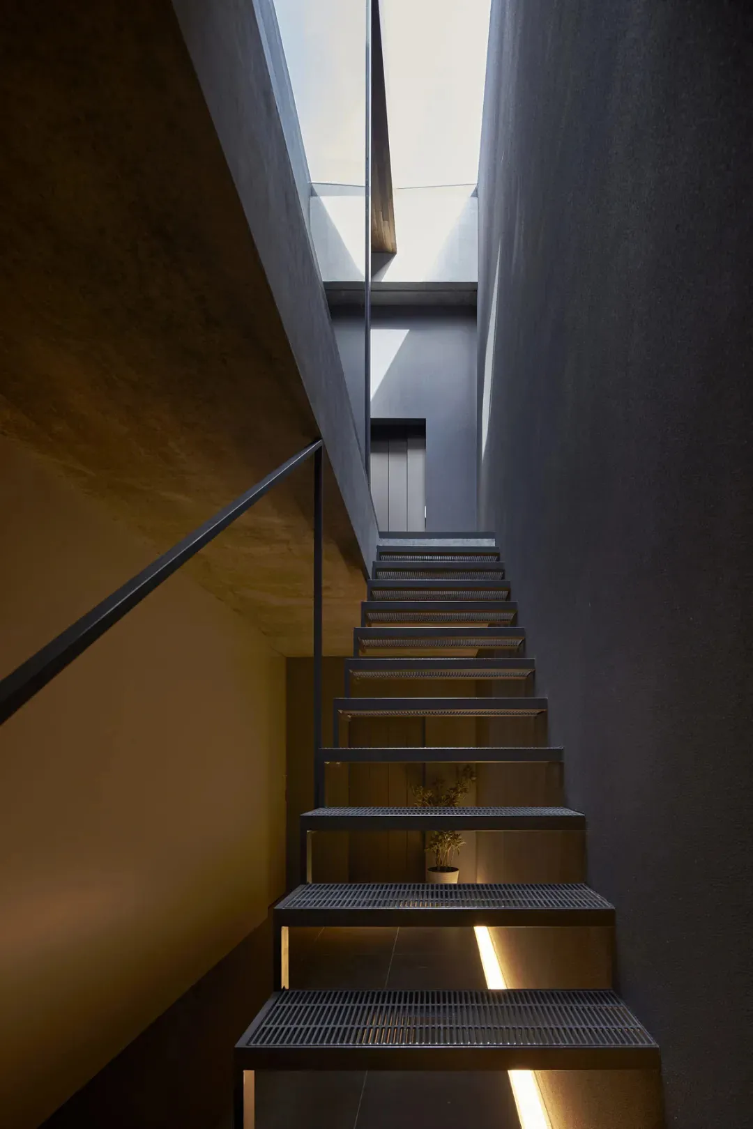 A minimalist staircase with a grid-like metal design and concrete steps, illuminated by soft lighting from below.