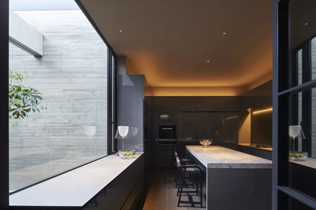 A sleek, modern kitchen features a minimalist design with concrete finishes and a polished, reflective island.