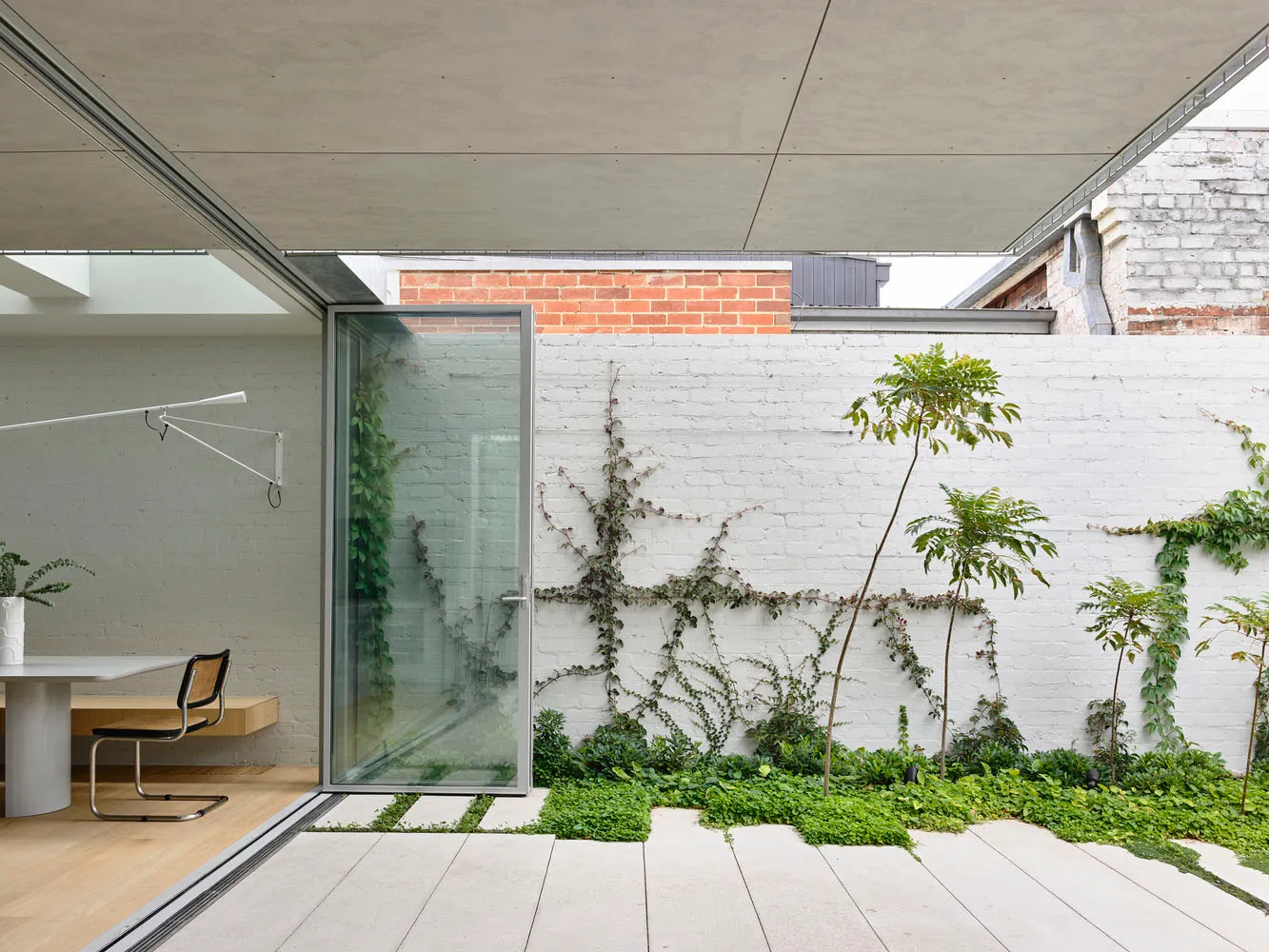 Modern architectural design featuring a white brick wall with concrete flooring and a vine-covered garden.