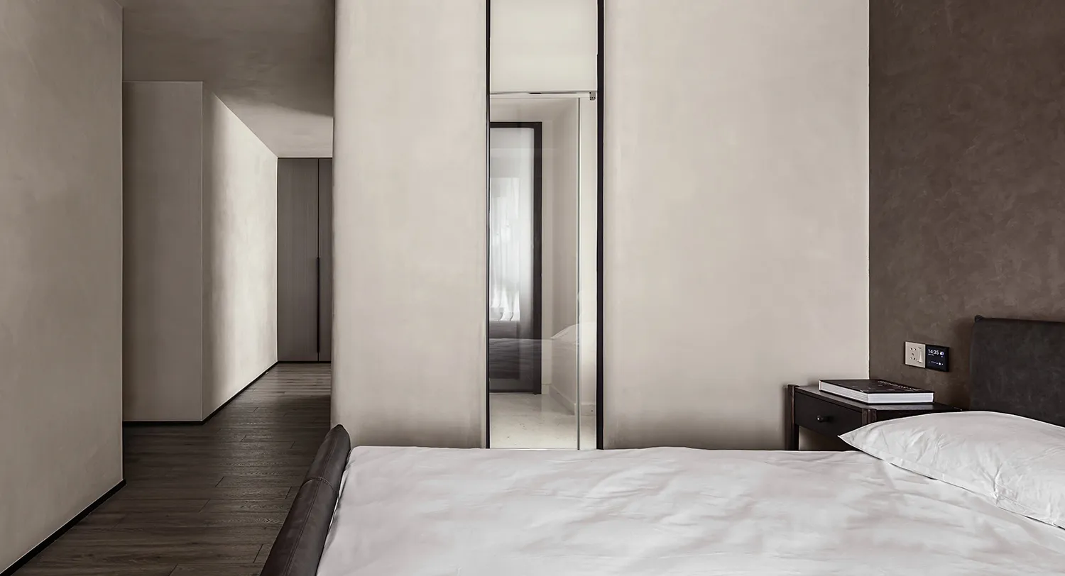 A modern minimalist bedroom featuring a white blanket and sheets, with a simple white bed against a light-colored wall.