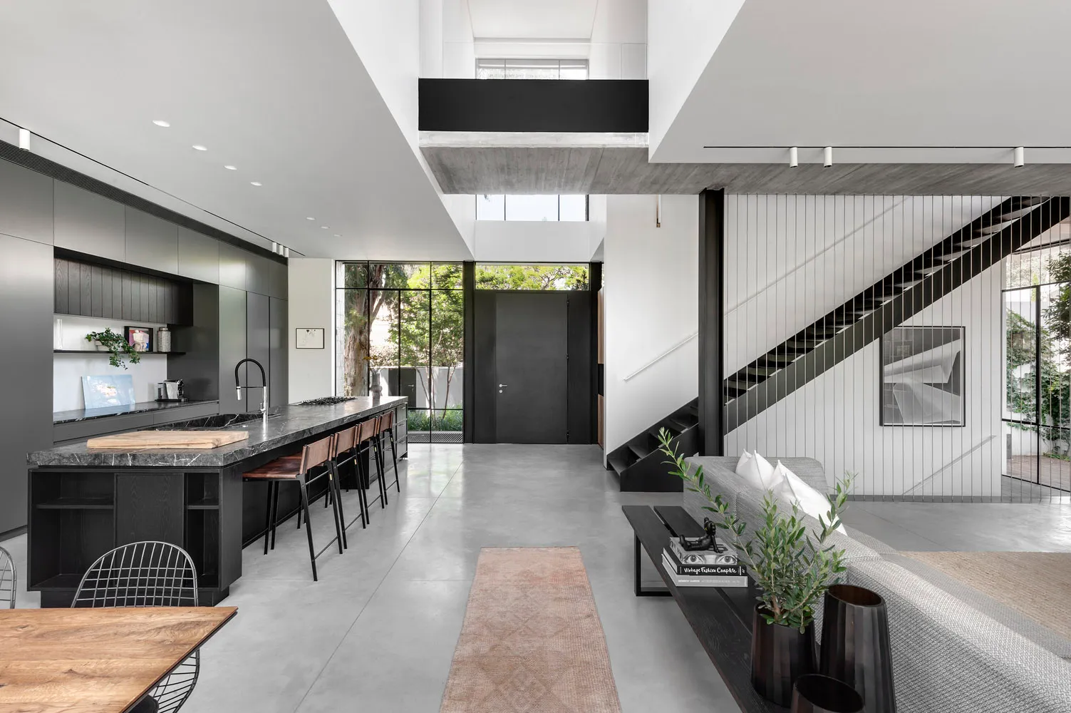 A modern interior living space with concrete flooring, a black kitchen island, and a staircase with a black railing.