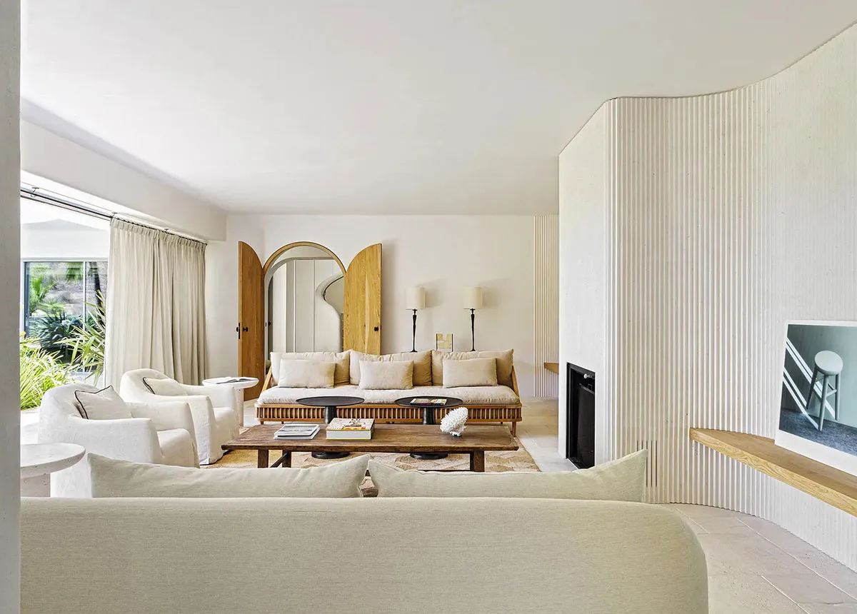 A modern living room featuring a wooden sofa, fabric armchairs, and concrete flooring with a wooden coffee table and white de