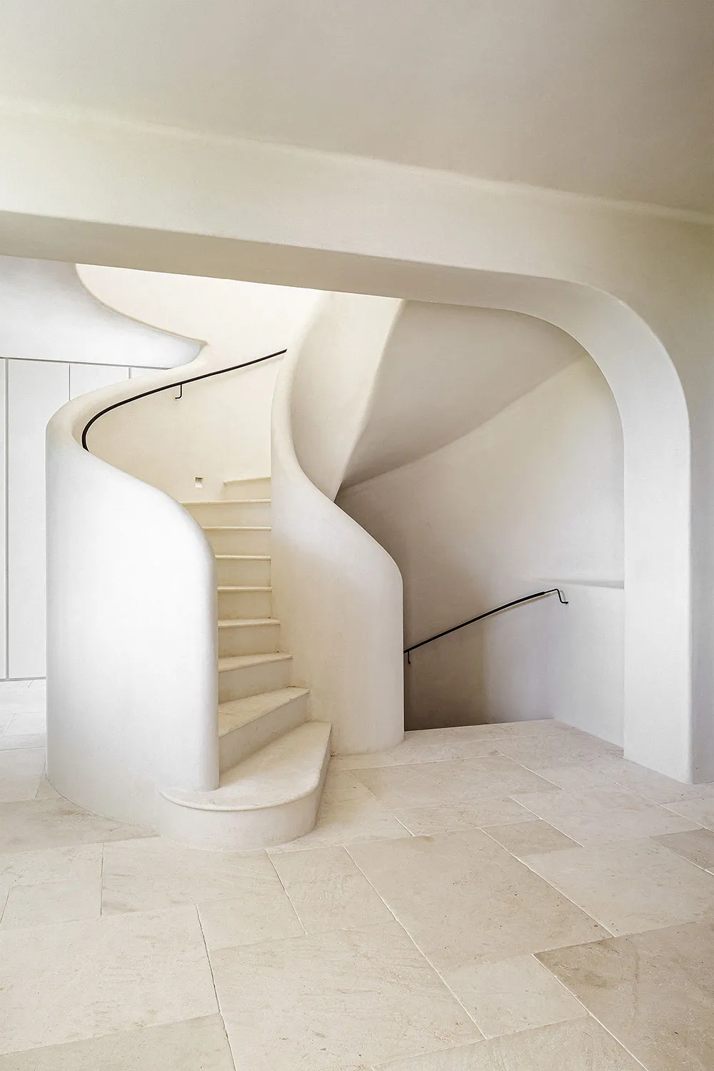 A modern, white stone staircase with curved walls and railings.