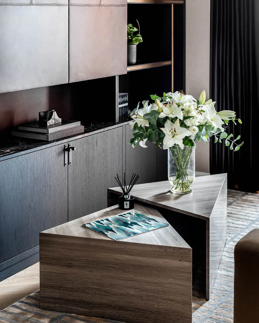 Modern coffee table adorned with a vase of white lilies and a scented stick diffuser on a wooden base.