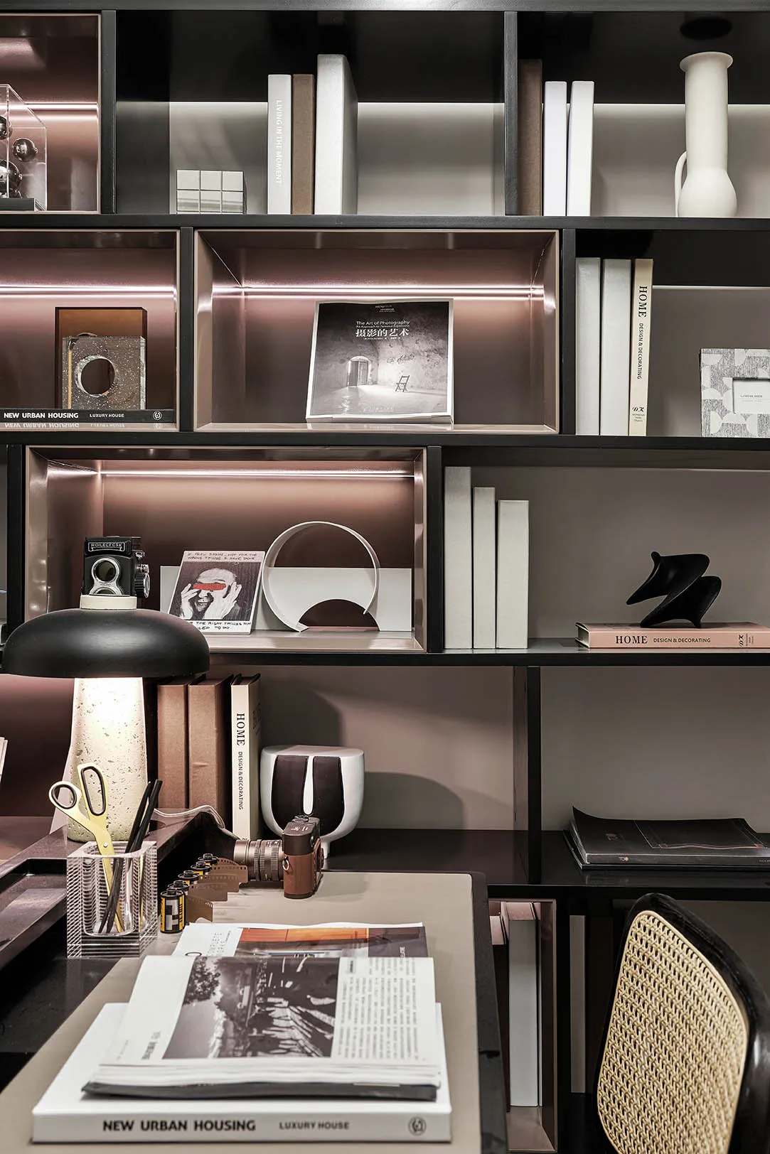 A modern home office with black furniture and white walls, featuring a desk, shelves with books, a desk lamp, and decorative 