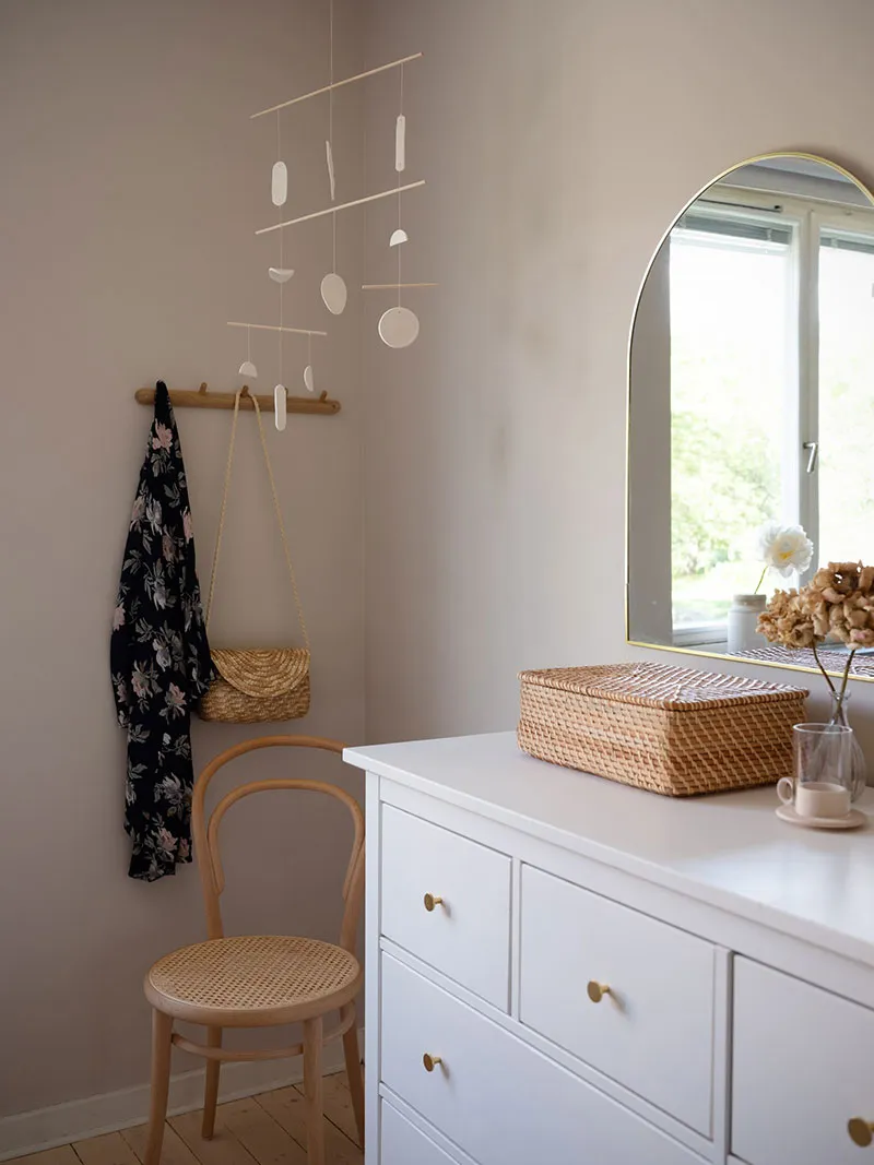 A minimalistic residential interior with a white dresser, a wooden chair, and a rattan basket.