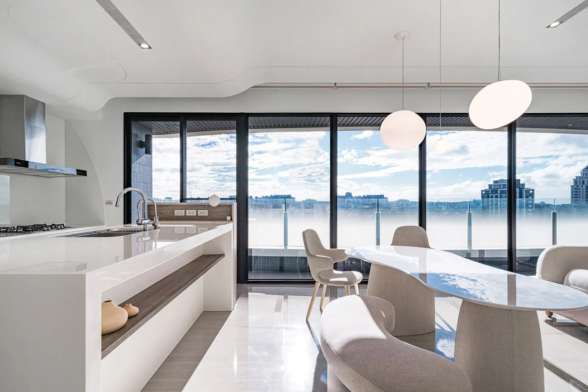 An elegant, modern residential kitchen with a white countertop and glass walls.