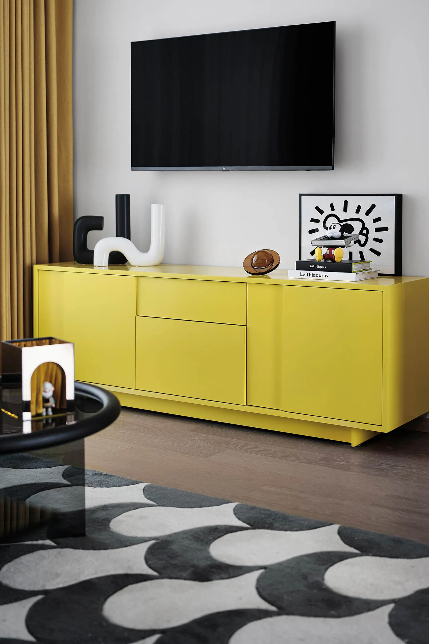 A modern living room featuring a bright yellow cabinet, a TV mounted on the wall, and various decorative items.