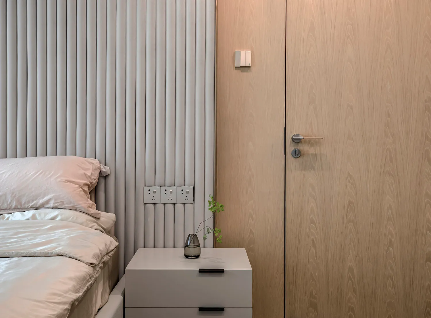 Minimalist bedroom with a wooden wall and fabric headboard, featuring a bedside table with a vase.