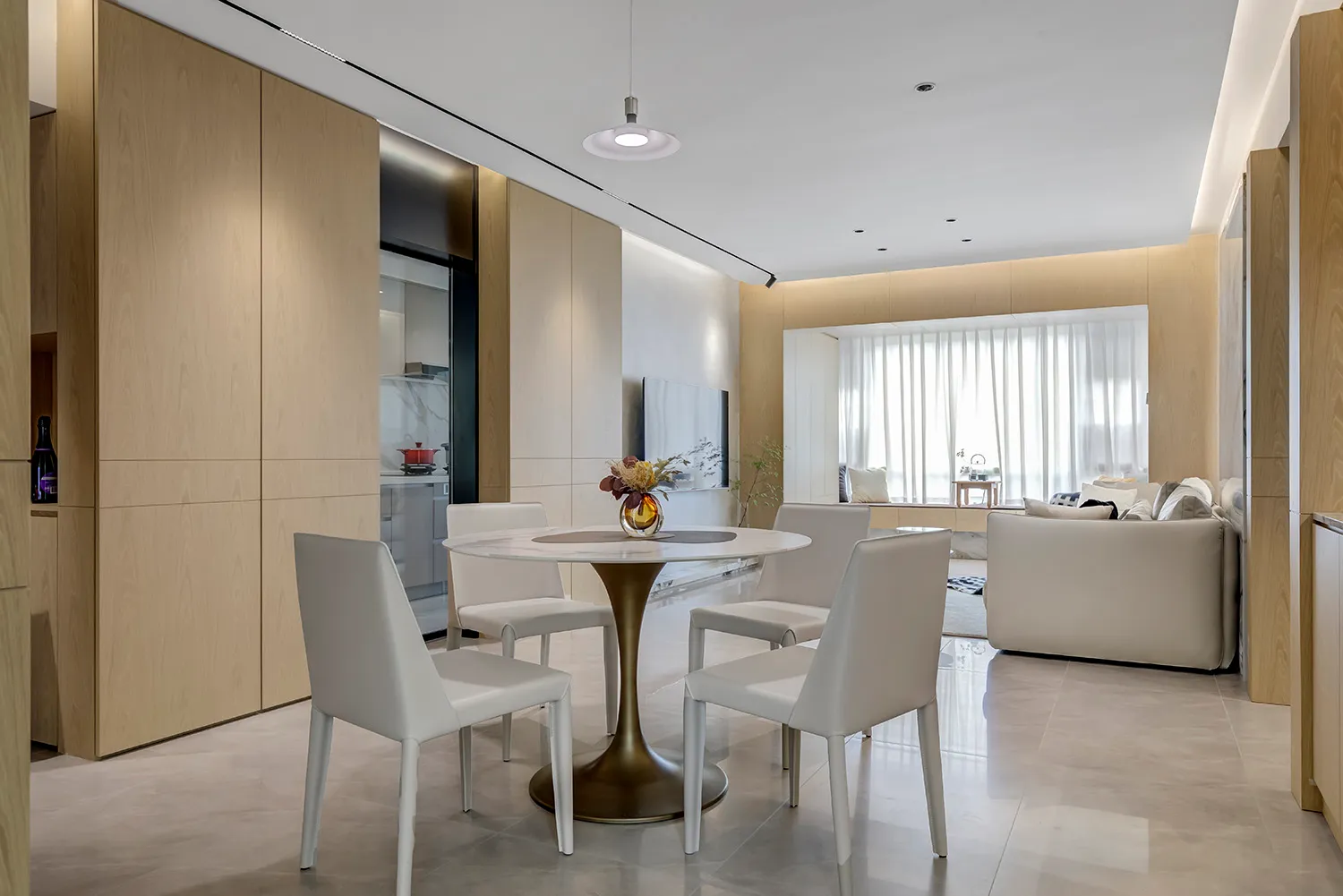Modern dining room featuring a round marble table surrounded by white leather chairs, integrated with a kitchen area and a li