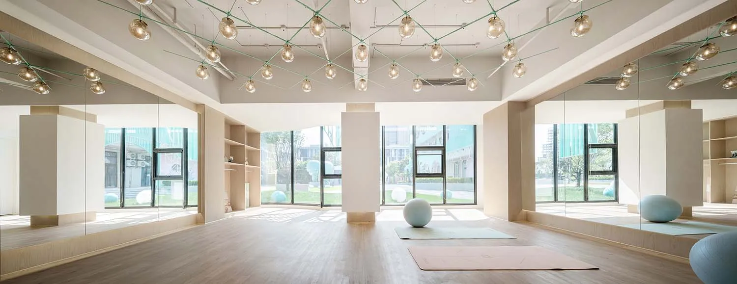 An spacious interior of a minimalist fitness-studio with wooden floors, mirrored walls, glass windows, and exercise equipment