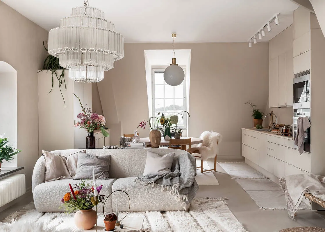 A minimalist living room with neutral tones, featuring a white sofa, white rug, and white walls with a large window.