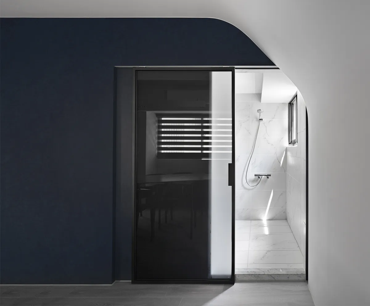 Minimalist modern bathroom with marble walls, glass shower enclosure, and wooden floor.