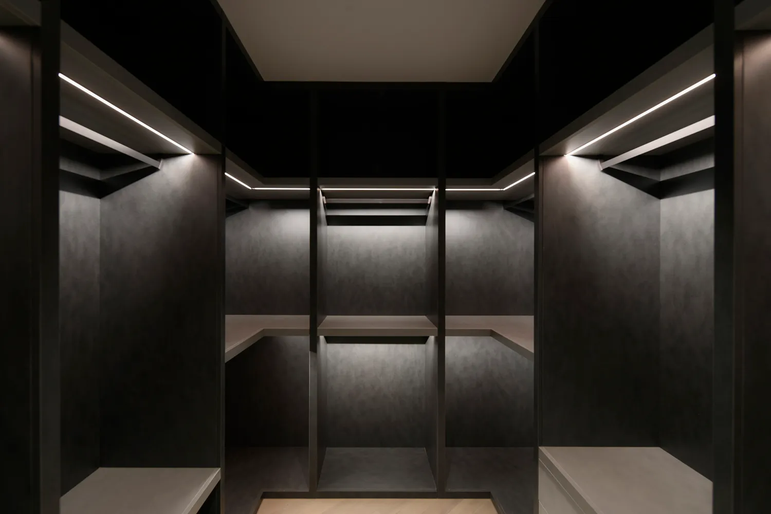 An empty, minimalist closet with concrete walls and shelves illuminated by embedded lighting.