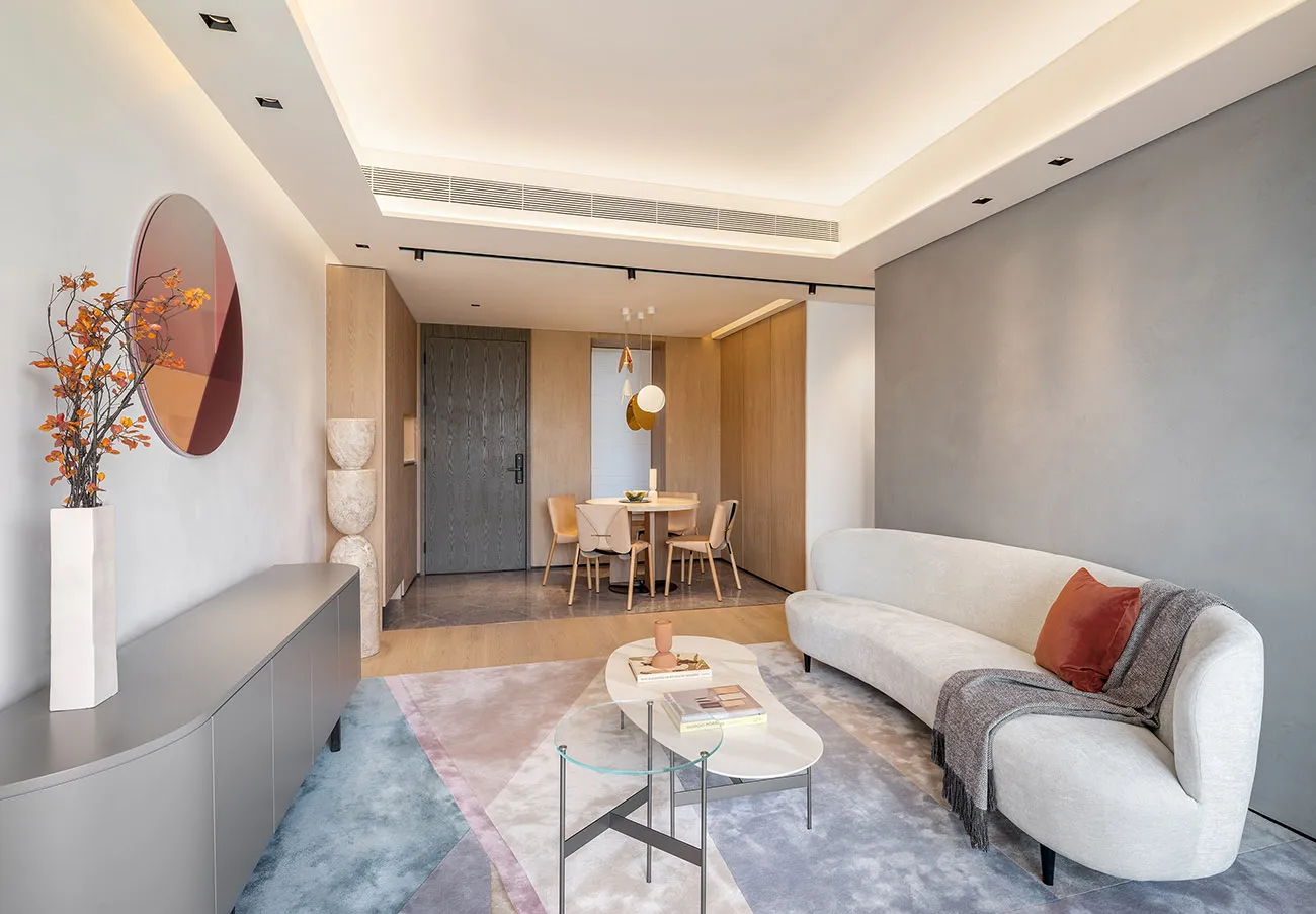 Modern minimalist living room with white furniture, grey walls, and a grey floor with a pastel-colored rug.