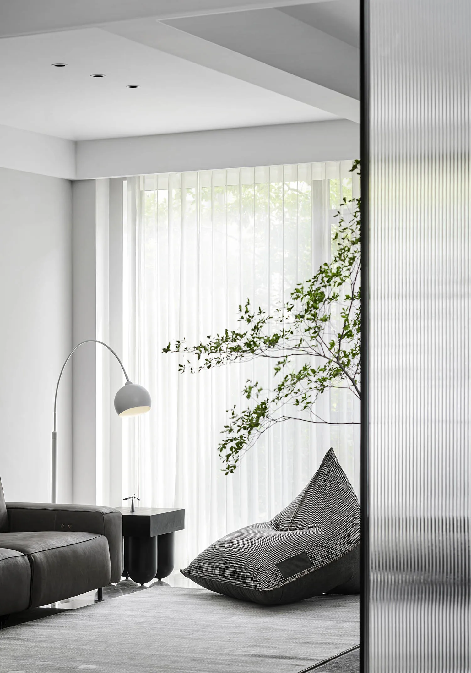 Modern minimalist living room featuring a grey couch, white curtains, and a plant in the corner.