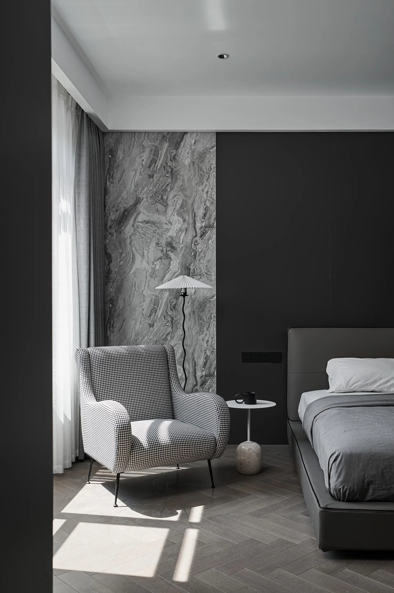 A modern bedroom featuring a bed with a marble headboard, a fabric chair, and wooden flooring.