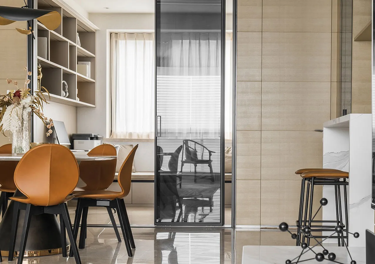 A modern living and dining room with beige tiled walls, wooden furniture, and glass doors.