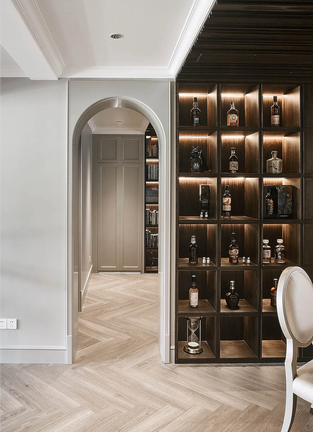 A modern bar with wooden shelves displaying various bottles and a decorative hourglass.