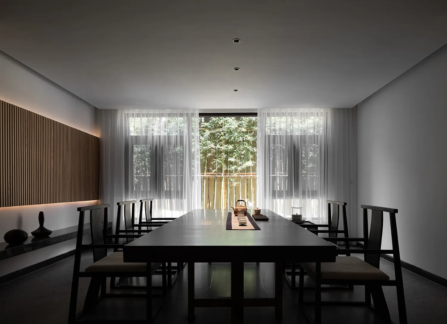 A modern minimalist restaurant dining room with a long table, chairs, and a tea ceremony setting.