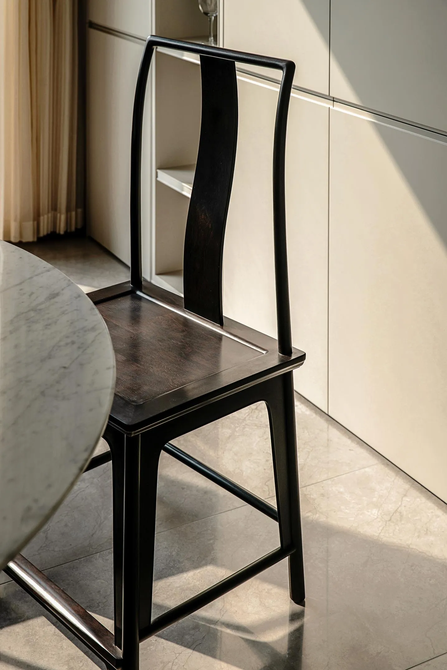 A black dining chair with a curved, high-back design next to a marble floor.