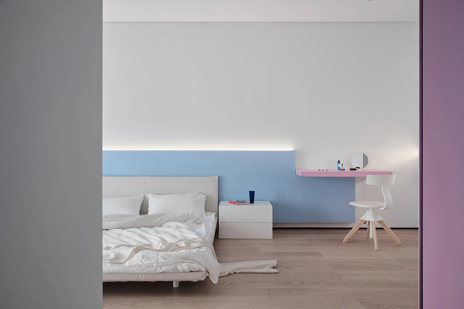 A modern minimalist bedroom with white bedding, a floating desk, and a simple design aesthetic.