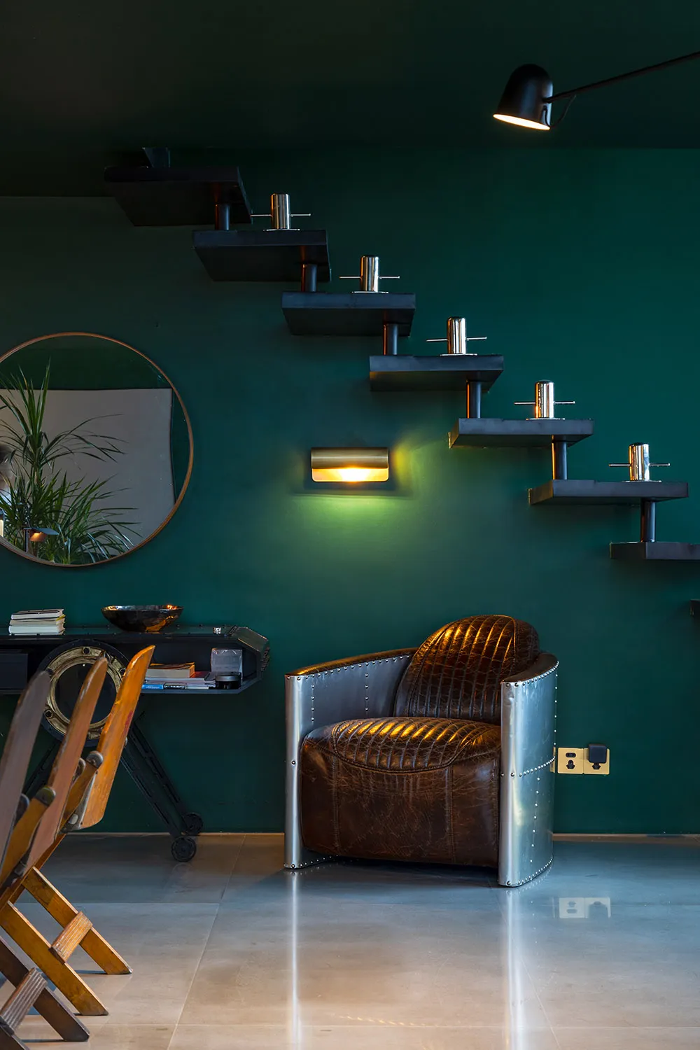 A minimalist living room with a dark green wall, black shelves, and a brown leather armchair.