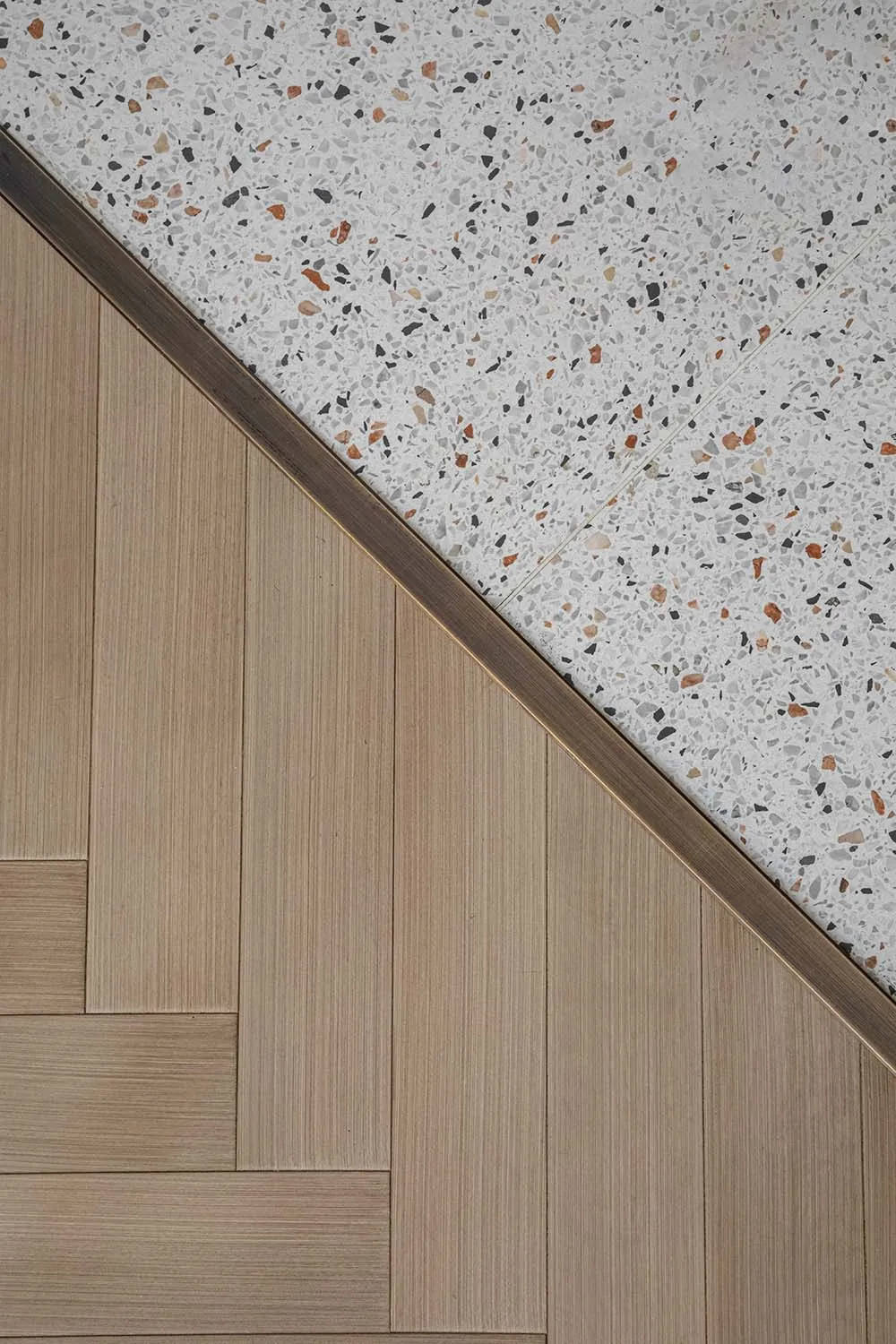 A modern floor featuring a wood pattern with a contrasting terrazzo section bordered by a bronze metal strip.