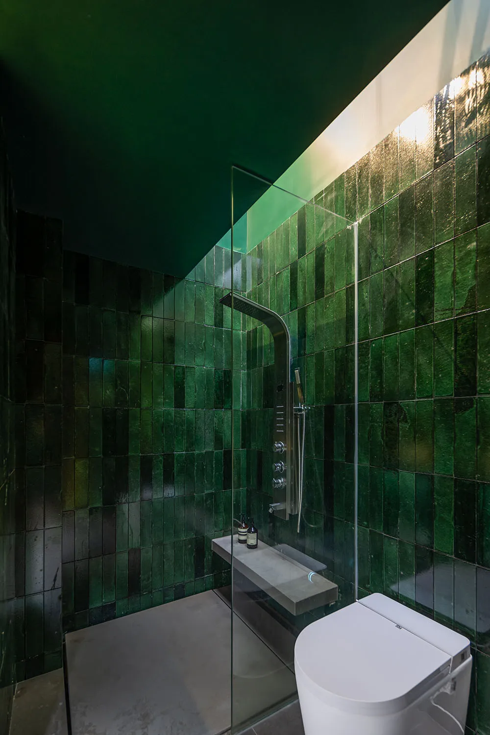 A modern bathroom featuring green tiles and a glass shower enclosure.