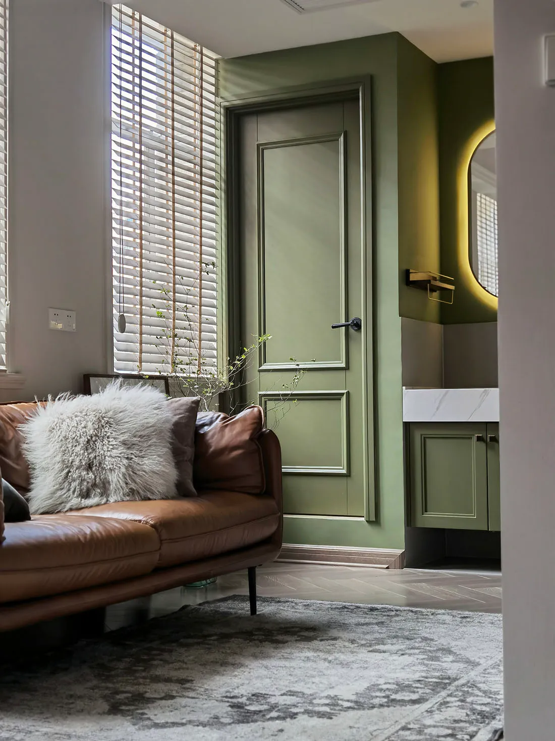 Modern living room featuring a leather sofa and green-painted wooden door, complemented by marble accents.