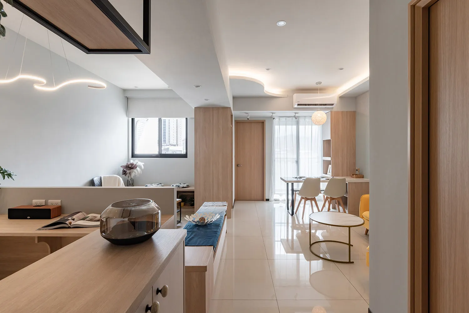 A modern residential kitchen and dining room featuring soft laminate flooring, white furniture, and natural light.