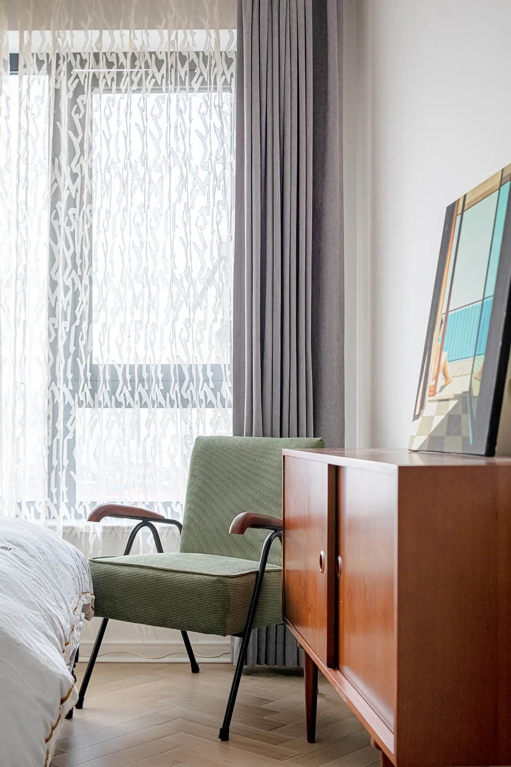 A modern bedroom with a green accent chair and fabric curtains by the window.