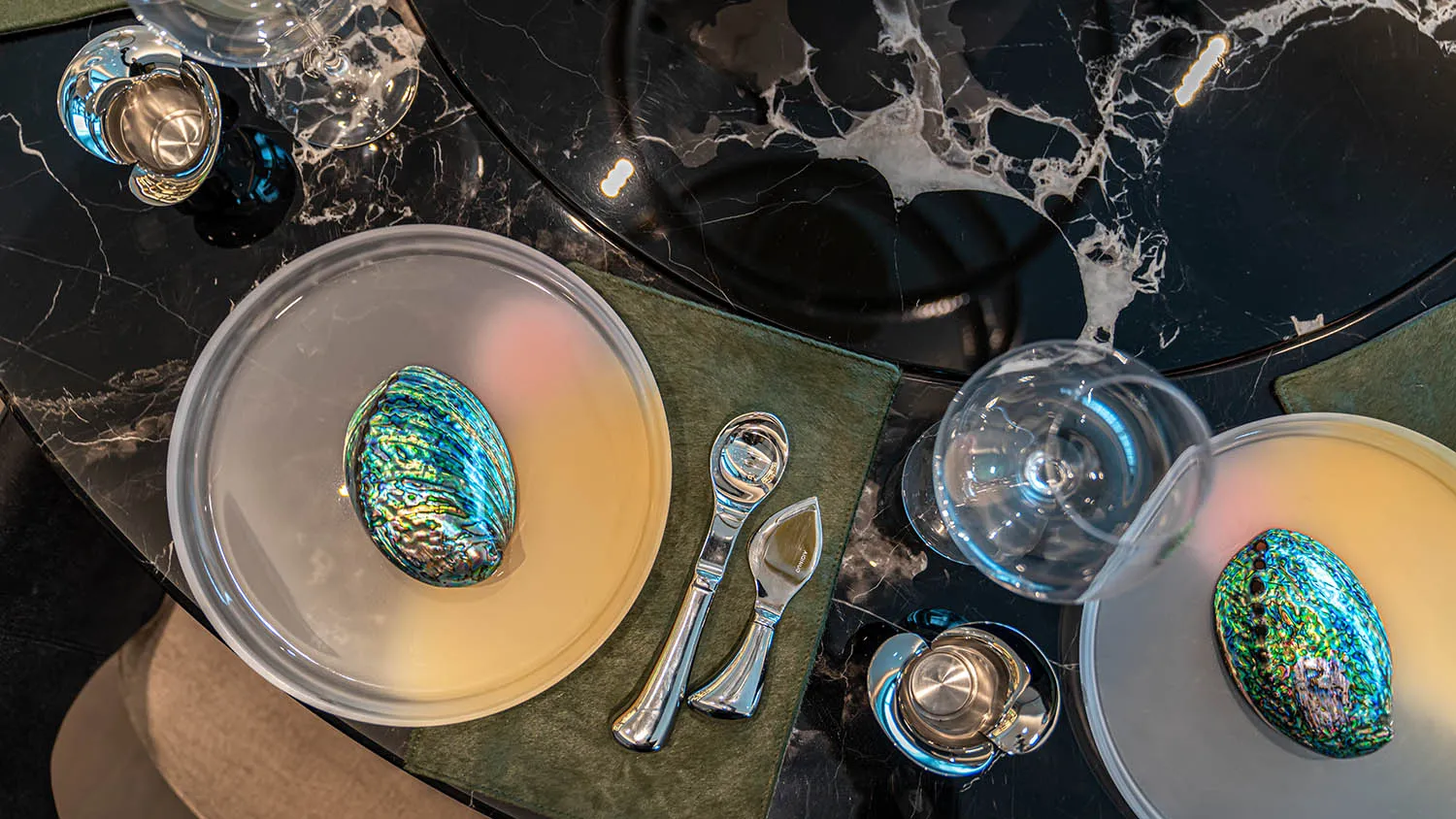 Modern dining table with marble top, two glass wine glasses, and a metallic serving dish with a blue shell inside.